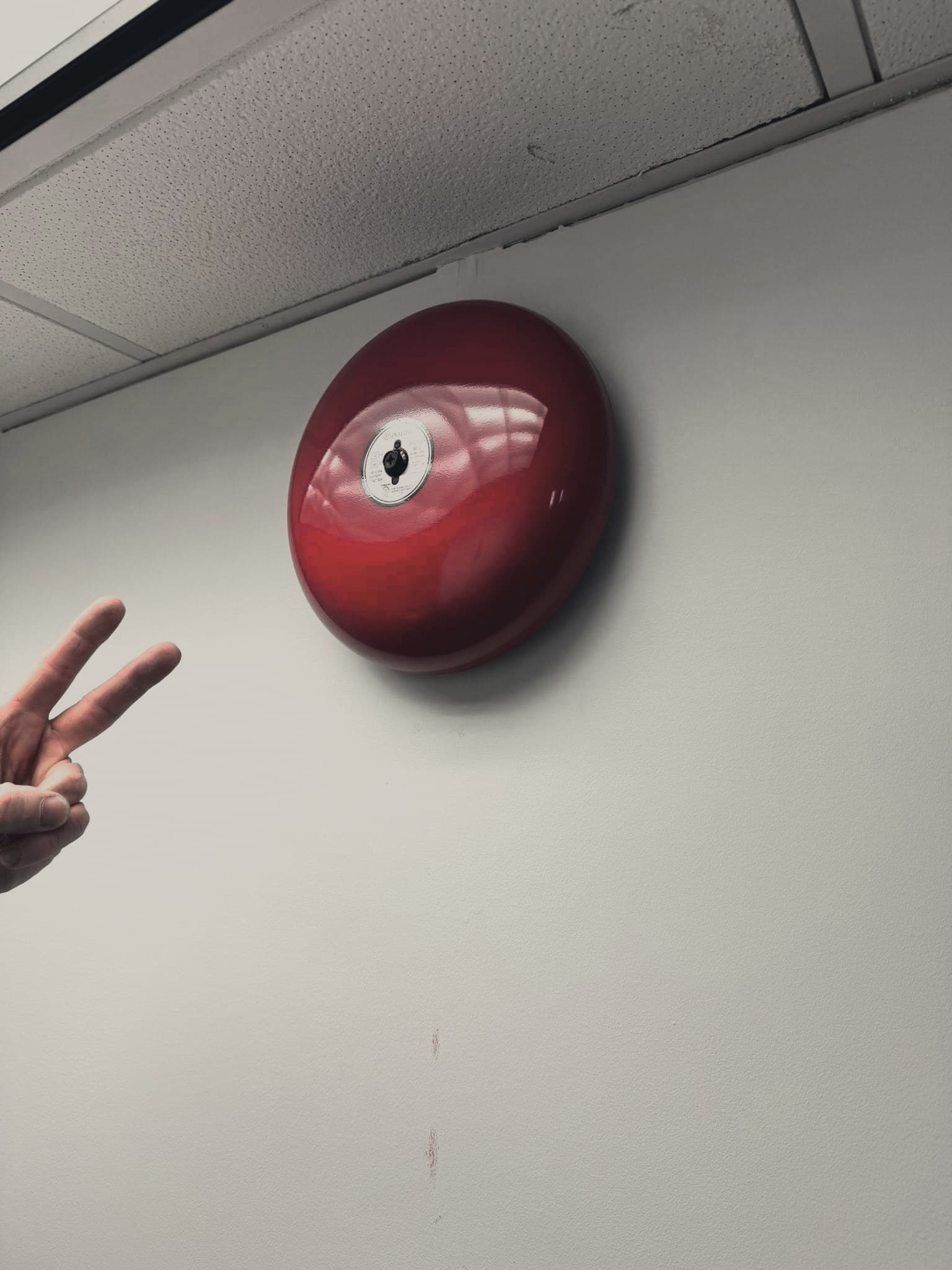 A red fire alarm bell mounted on a wall.
